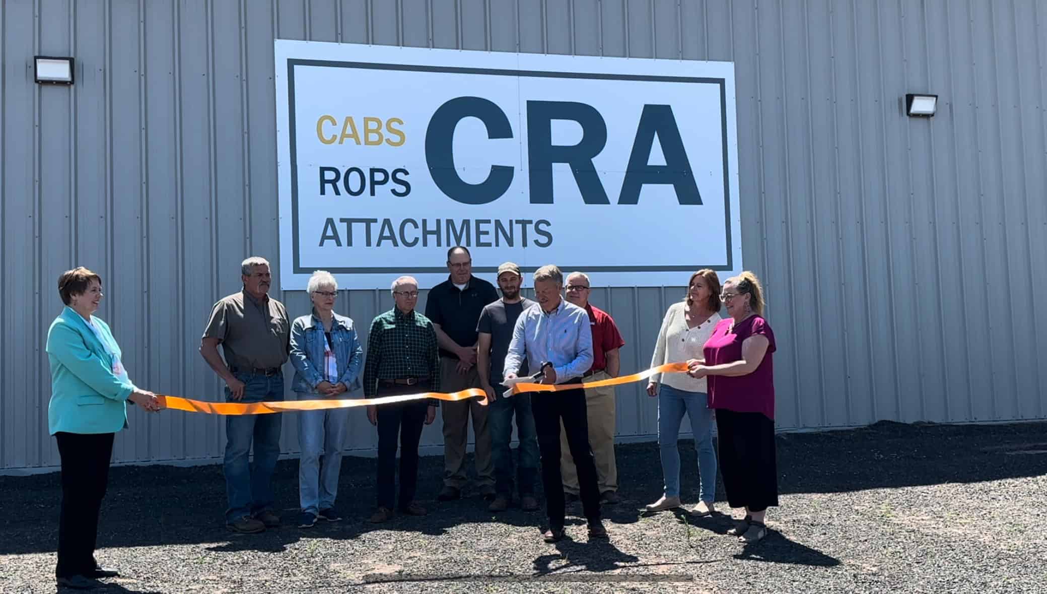 Several people gather in front of a building marked with a sign that says "CRA," showcasing a ribbon cutting ceremony with community